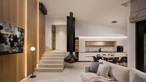 Una sala de estar moderna con un sofá, una mesa de centro y una chimenea. Se ve una escalera que conduce a un nivel superior con una zona de cocina.