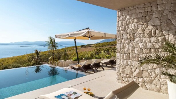 Un área junto a la piscina con pared de piedra, sillas de descanso y una sombrilla.