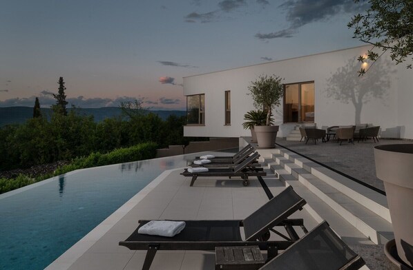 Ein moderner Poolbereich im Freien mit Liegestühlen, einem Blumentopf und Blick auf die Berge.