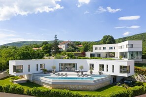 Ein modernes, zweistöckiges Haus mit Swimmingpool, Sitzgelegenheiten im Freien und Blick auf die umliegenden Hügel.