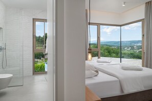 Ein modernes Hotelzimmer mit Dusche, Toilette und einem Bett mit Blick auf die Landschaft.