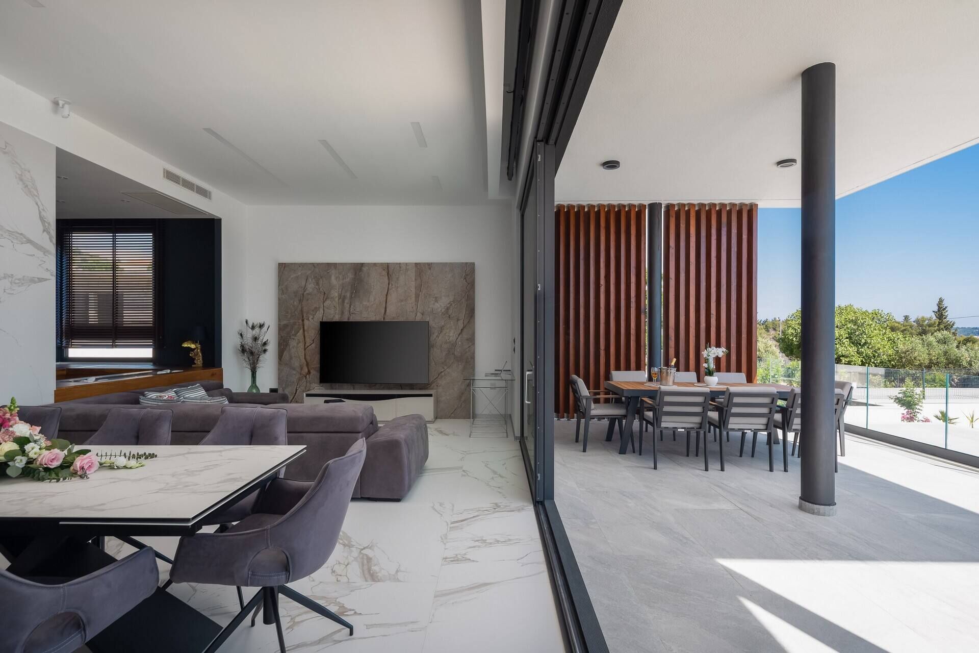 A modern living room with a large TV, comfortable seating, and a balcony with a view.