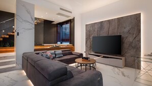 A modern living room with a sectional sofa, a flat-screen TV mounted on a marble wall, and a small round table with a book. - Luxury Villa Excellence with a pool (Seget Vranjica)