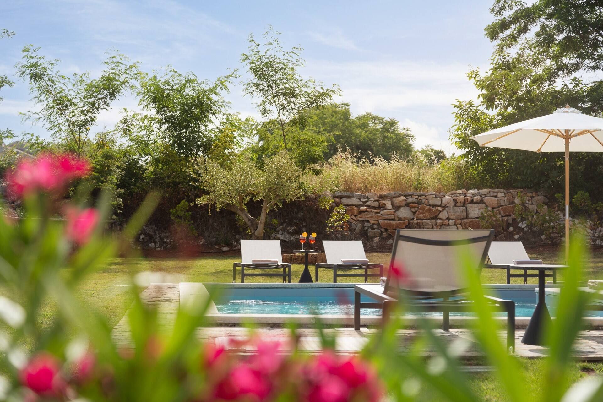 Un área junto a la piscina con sillas de descanso y un muro de piedra.