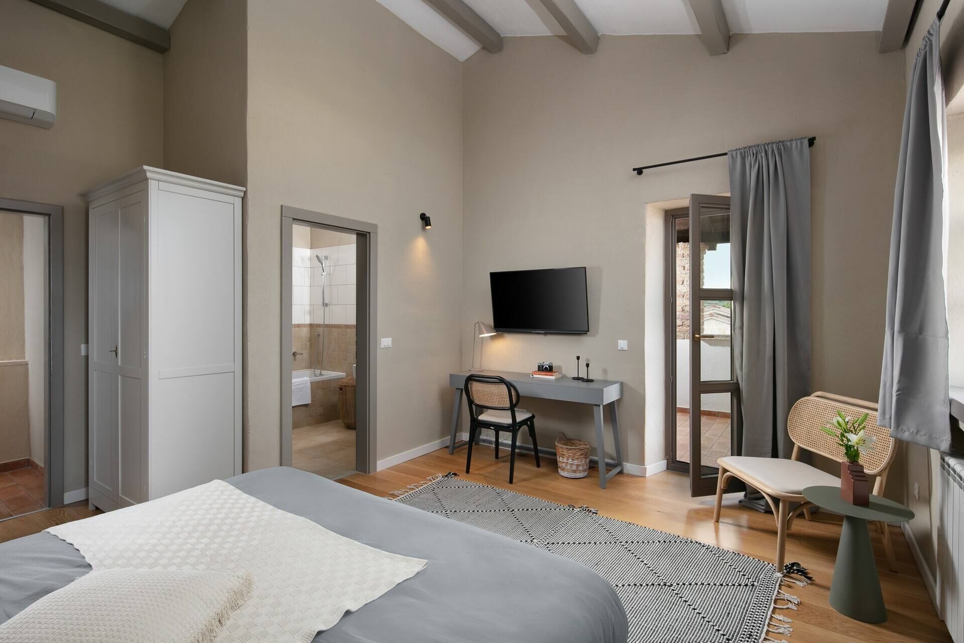 A bedroom with a bed, a desk, a chair, a TV, and a window with curtains.