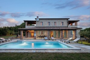 A two-story stone house with a swimming pool, outdoor seating, and a covered patio.