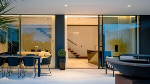 A modern interior with a dining area, a staircase, and a view through large glass doors.