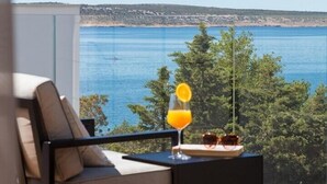 A balcony with a view of the sea, a chair, a table with a glass of orange juice, and a potted plant.