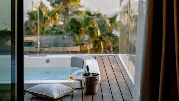 A balcony with a hot tub, a glass partition, a cushion, and a wine glass with a bottle.