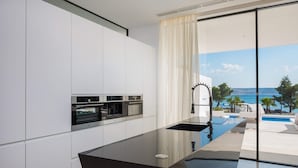 A modern kitchen with built-in ovens and a sleek black countertop, overlooking a pool and a scenic view.