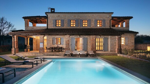 A two-story stone house with a swimming pool, outdoor seating, and a covered patio area.