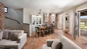 A spacious living area with a dining table and chairs, a sofa, and a kitchen area with a brick wall and white cabinets.