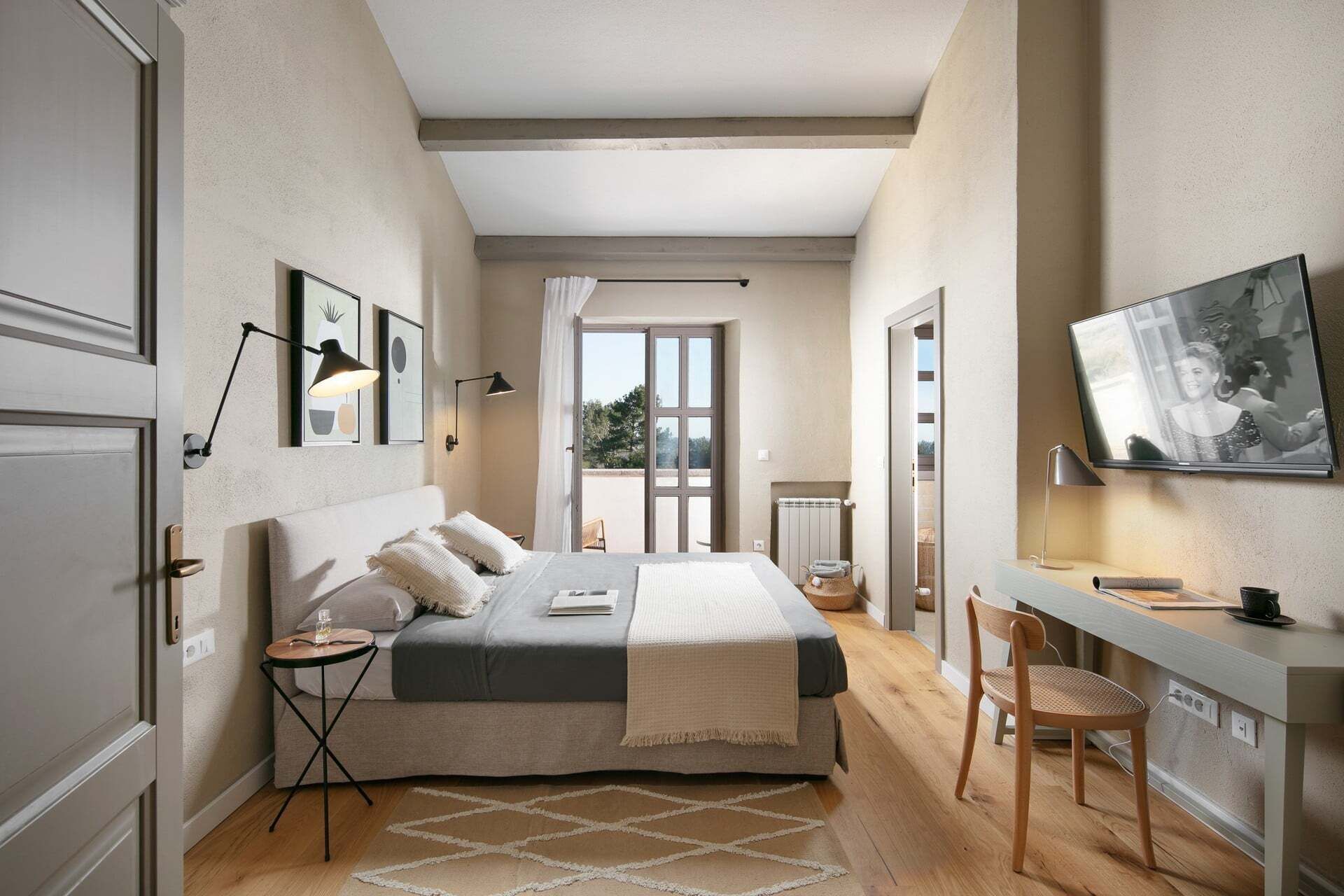 A bedroom with a bed, bedside tables, a desk, a chair, and a television.