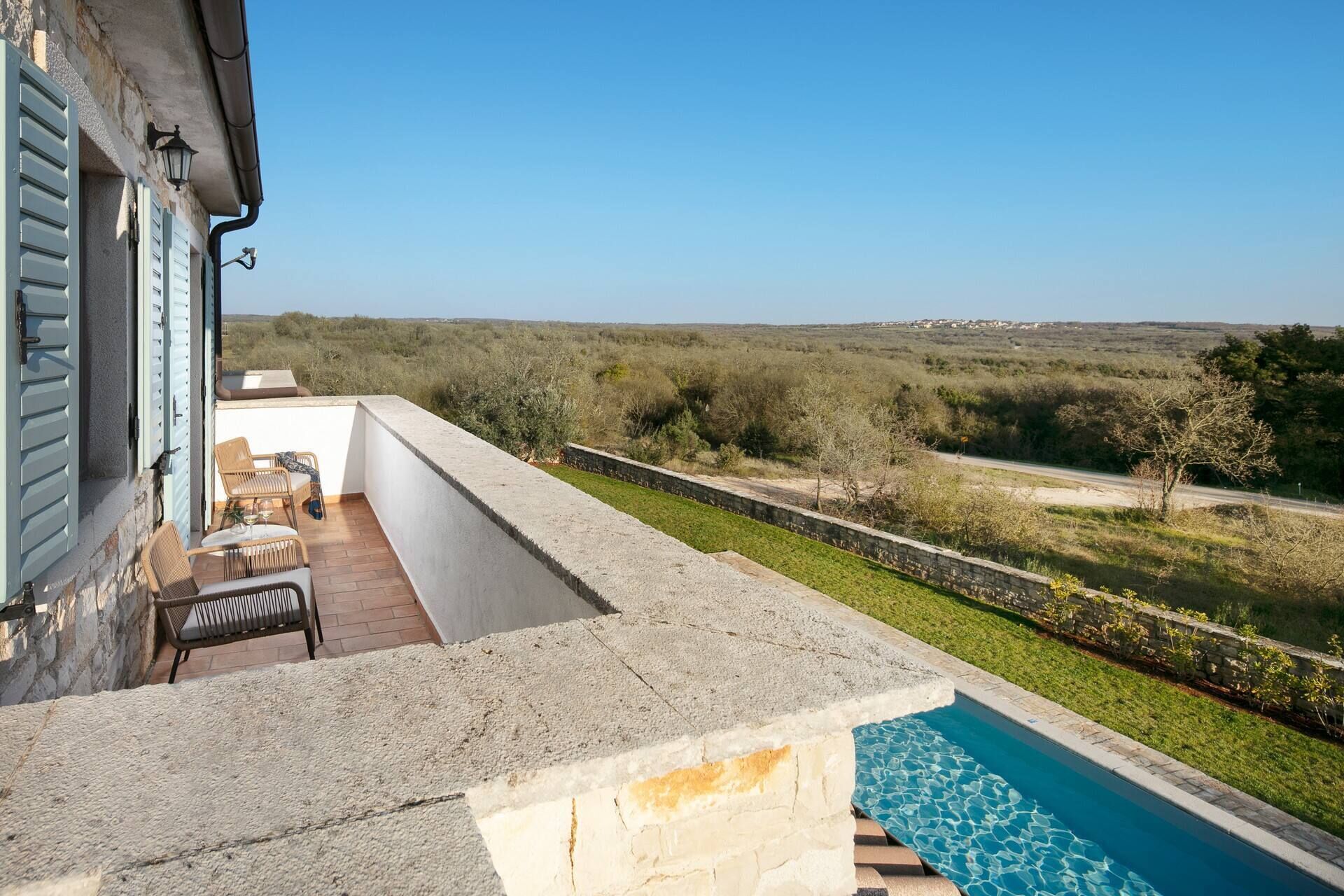A balcony with a pool, outdoor furniture, and a view of the countryside.