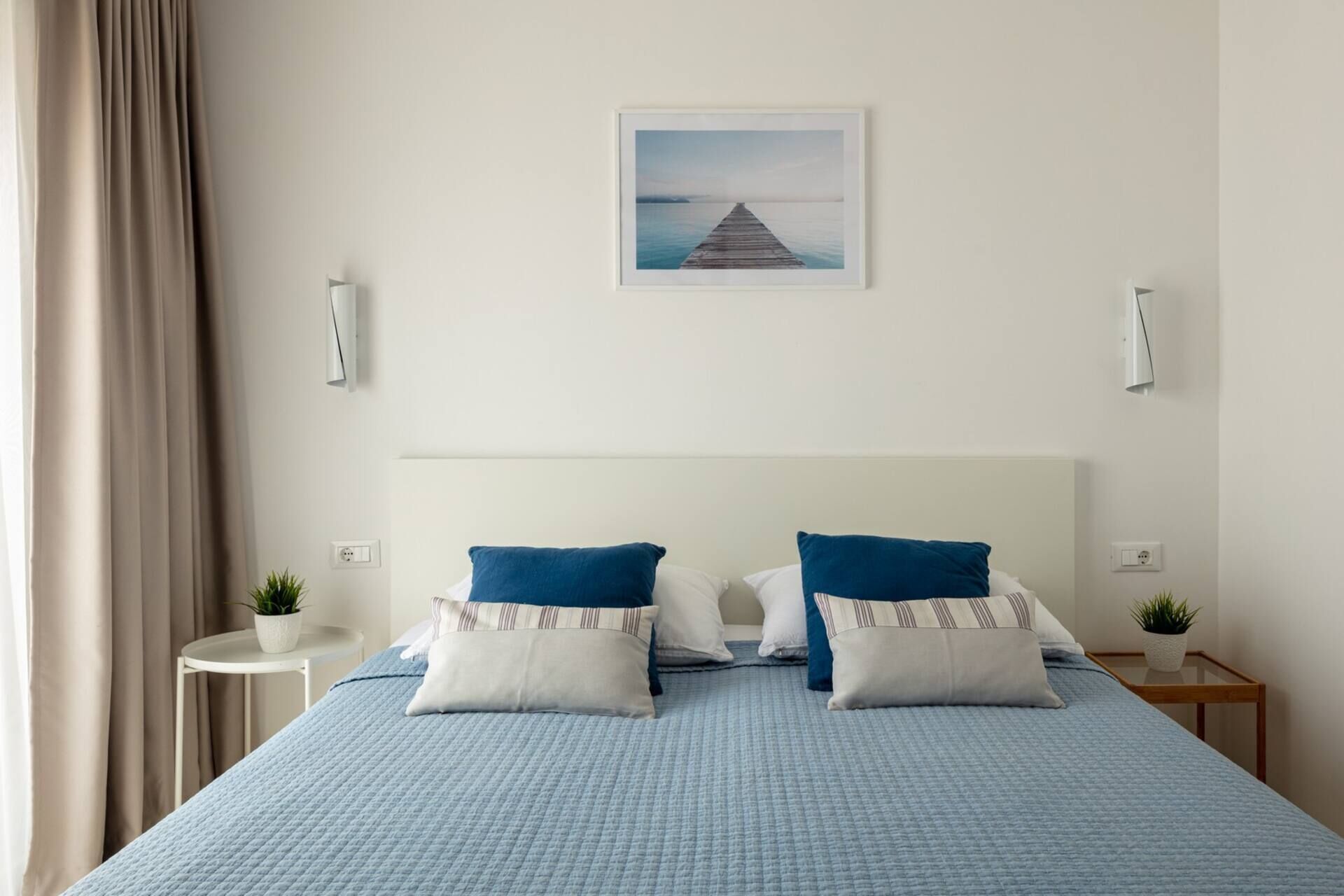 Ein Hotelzimmer mit einem Bett, zwei Nachttischen, einem Wandbild und einem Fenster mit Vorhängen.