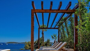 A wooden pergola with lounge chairs overlooking a pool and the sea. - Villa Crystalsea 1 infinity heatedpool in Hvar in Hvar, sauna, family, stylish, sea view (Hvar)