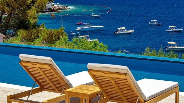 A poolside area with two wooden lounge chairs and a view of the sea with boats. - Villa Crystalsea 1 infinity heatedpool in Hvar in Hvar, sauna, family, stylish, sea view (Hvar)