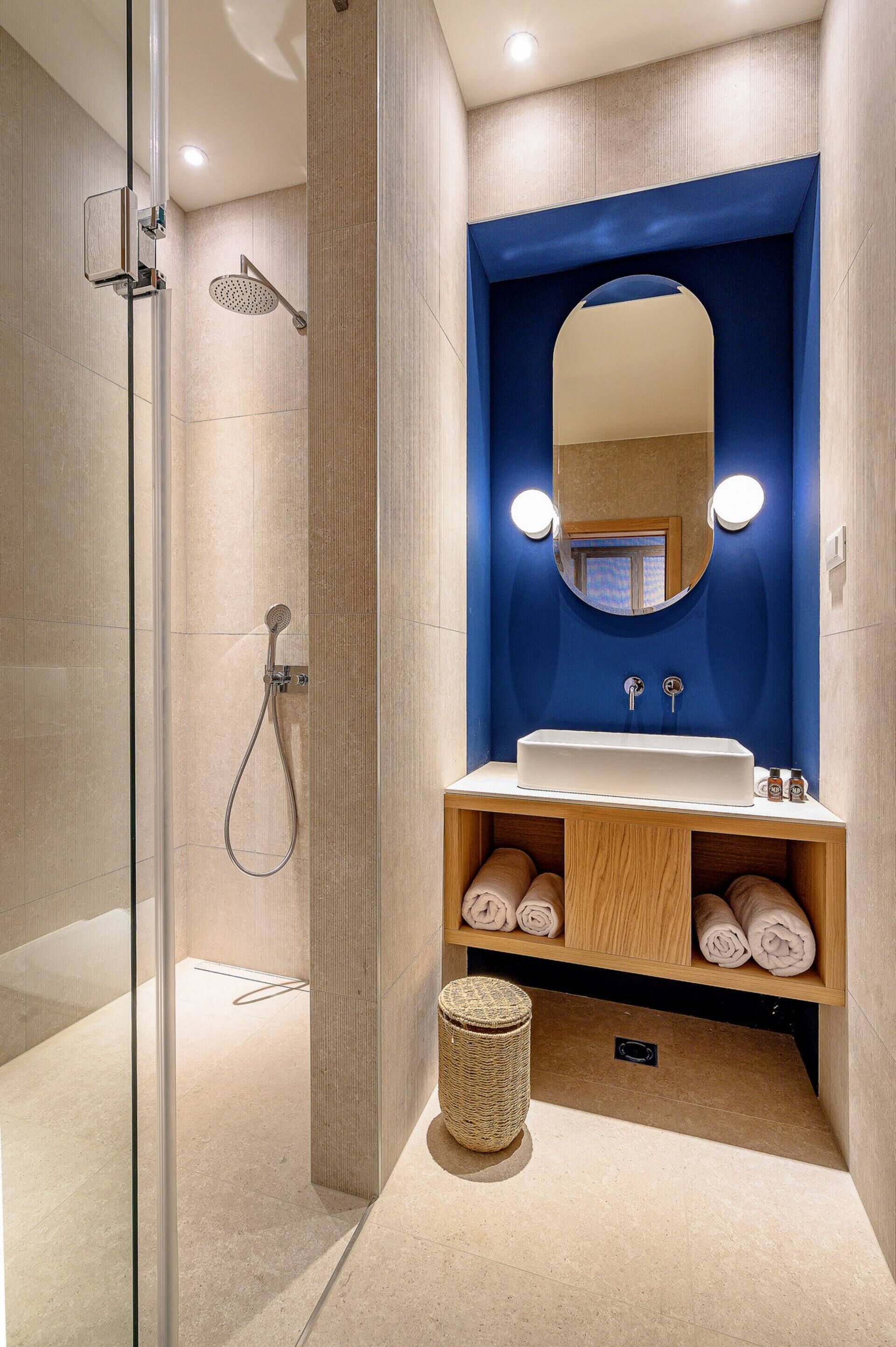 A modern bathroom with a glass shower enclosure, a wooden vanity with a white sink, and a blue accent wall.