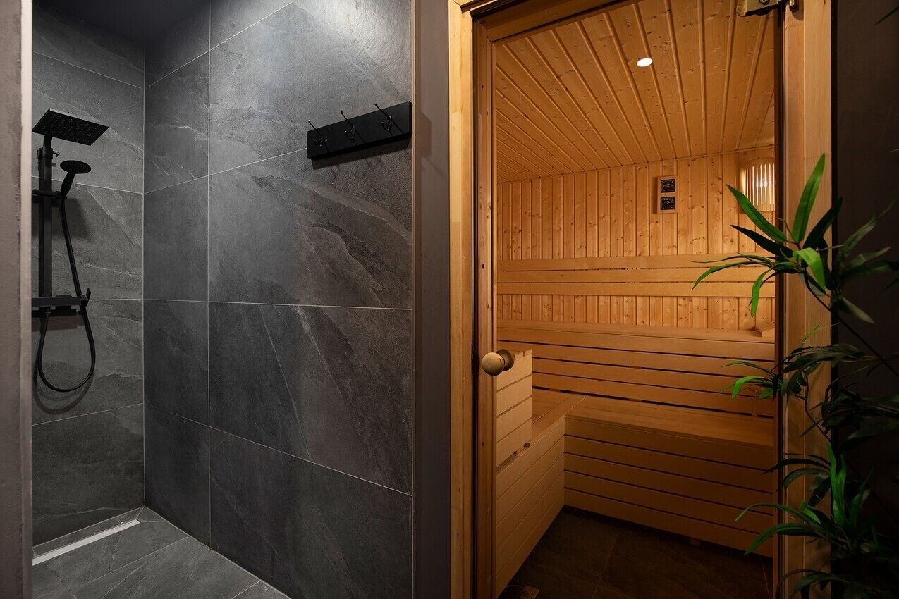 Et sauna-rum med mørke flisevægge og en trædør.