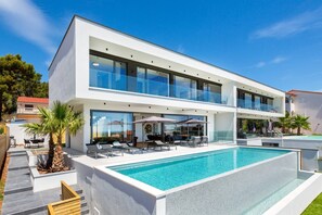 A modern two-story house with a large swimming pool, outdoor seating, and a clear view of the surrounding area. - Luxury Villa Dali - 42 m2 infinity pool & wellness, family, stylish (Medulin)