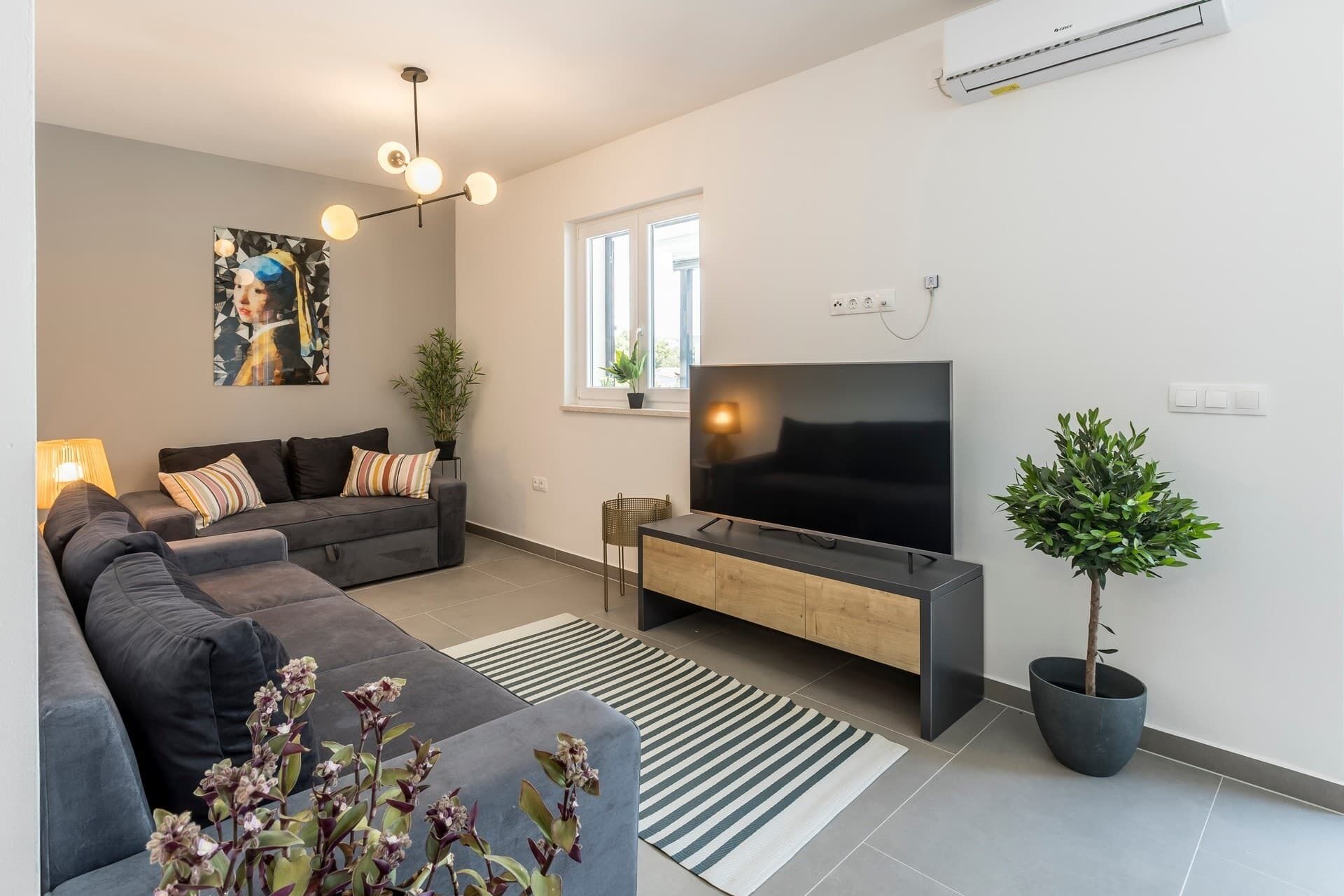 Un salon moderne avec un canapé d’angle, un téléviseur à écran plat, une table basse et une plante en pot.