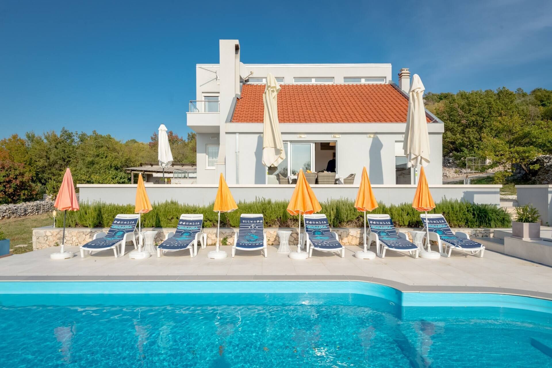 A modern hotel with a swimming pool, lounge chairs, and umbrellas.