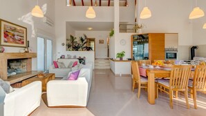 Un vaste espace de vie agrémenté d’une cheminée, d’une table à manger pour quatre personnes et d’une cuisine équipée d’appareils électroménagers modernes.