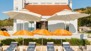 Un bâtiment moderne doté d’une piscine, de chaises longues et de parasols.