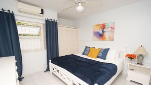 Un dormitorio con cama blanca, cortinas azul oscuro, ventilador de techo y aire acondicionado instalado en la pared.