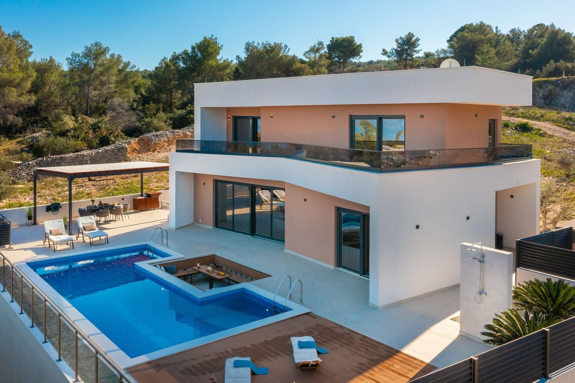 A modern two-story house with a swimming pool, outdoor seating, and a view of the surrounding landscape.