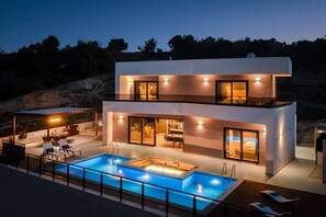 Una casa moderna a due piani con piscina, area salotto esterna e un balcone.