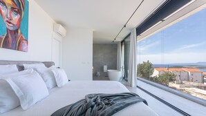 A modern hotel room with a large bed, a view of the city, and a painting on the wall.