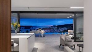 A modern interior with a dining area, a sofa, and a view of a coastal landscape.