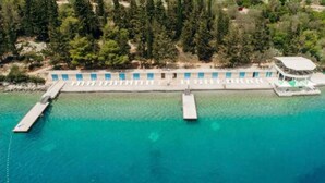 Eine Luftaufnahme eines Resorts mit einer langen Pier, die sich in türkisfarbenes Wasser erstreckt, umgeben von dichtem Grün.