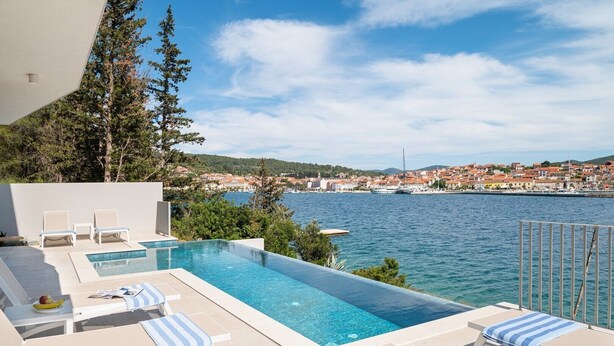 Ein Poolbereich mit Liegestühlen und Blick auf das Meer und die Stadt.