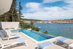 Un espace aménagé au bord de la piscine, avec des chaises longues et une vue sur la mer et la ville.