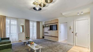 A modern living room with a sofa, a coffee table with fruit, a TV, and a door. - Terrace apartment Trocadero Eiffel Tower (Paris)