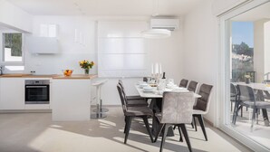 Une cuisine moderne avec des meubles blancs, un four encastré et un coin repas comprenant une grande table et des chaises.