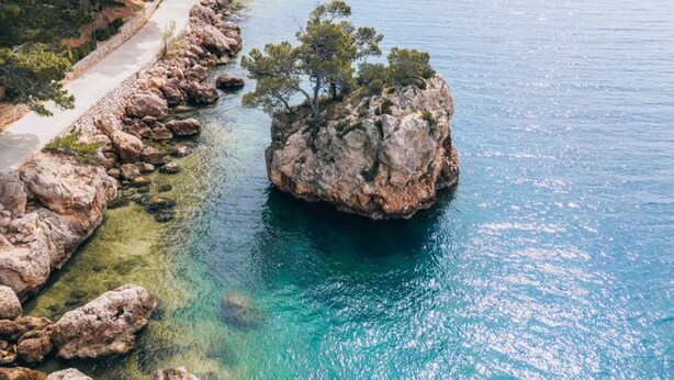 Un paysage côtier avec un promontoire rocheux entouré d’une eau bleue et limpide, une plage de sable et une végétation luxuriante.