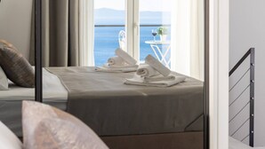 Une chambre d’hôtel avec un lit, une vue sur la mer et un balcon équipé d’une table et de chaises.
