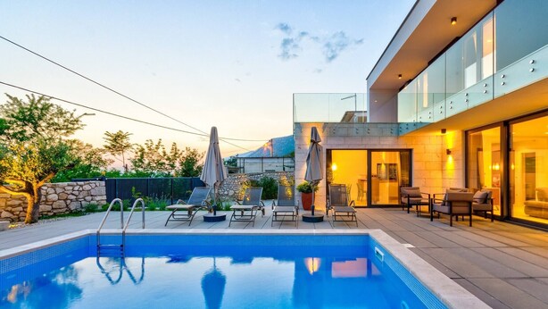 A modern pool area with lounge chairs and umbrellas, a stone wall, and a glass-enclosed patio with seating. - Excellent Villa Oasis with a pool, bbq, quiet area, family, gym (Grizane)
