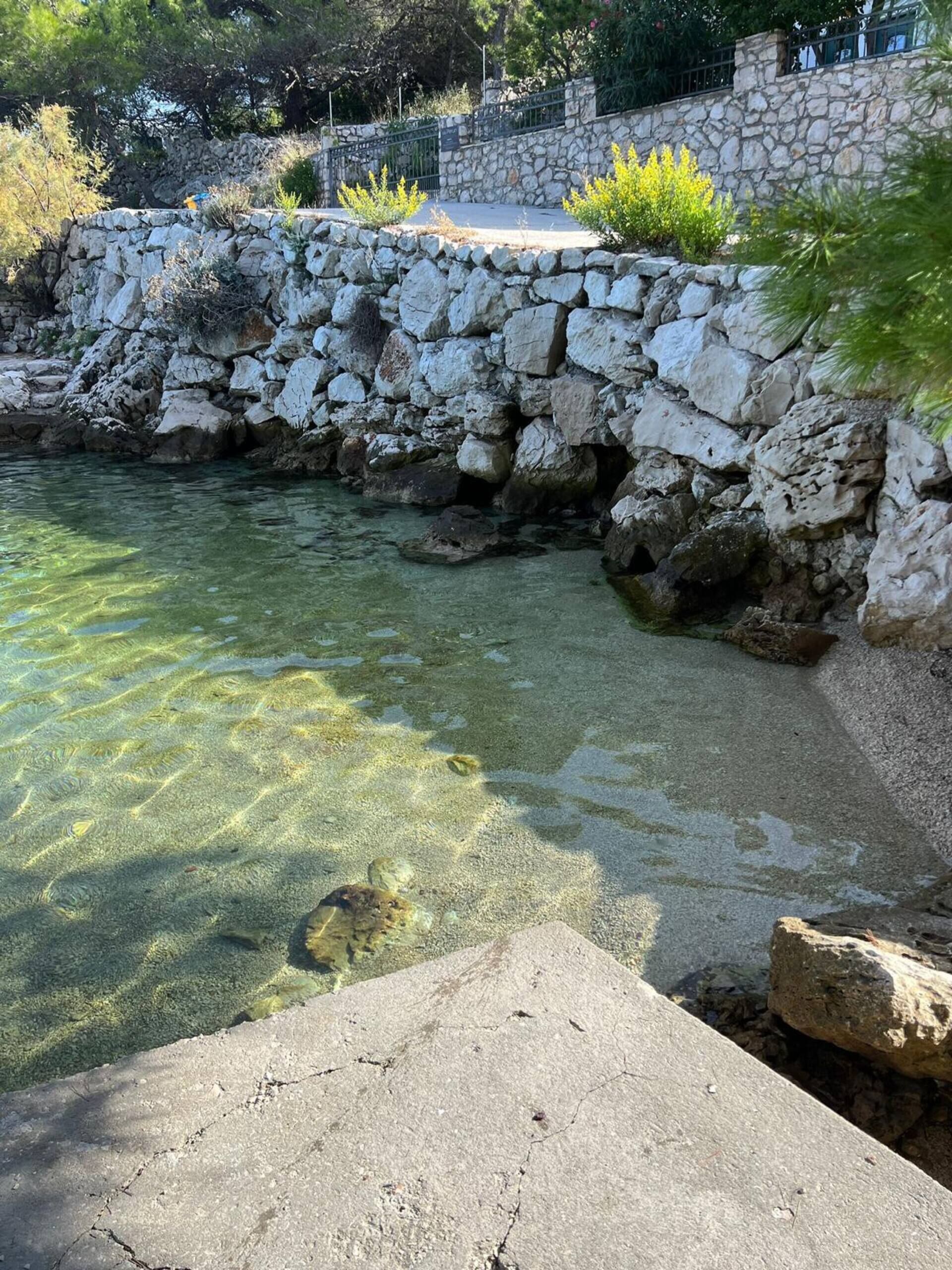 Un mur de soutènement en pierre bordant un bassin d’eau claire, le tout entouré de verdure et agrémenté d’un chemin pavé.