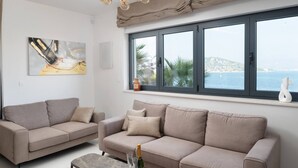 Un salon avec deux canapés beige, une table basse et une vue sur la mer grâce à de grandes fenêtres.