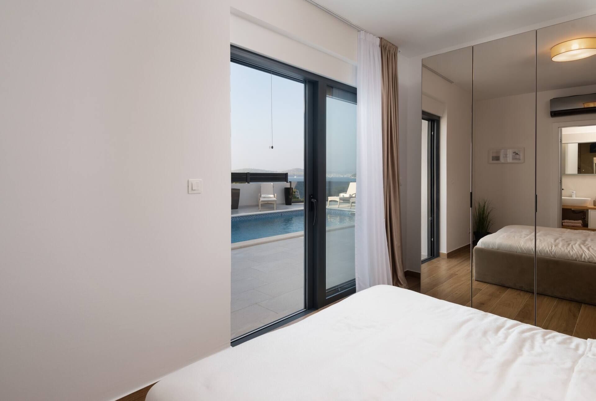 Une chambre d’hôtel moderne dotée d’une grande porte-fenêtre coulissante donnant sur un balcon avec piscine.