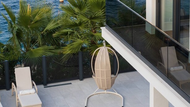 Un balcon moderne avec vue sur la mer, des fauteuils de salon blancs, une petite piscine et des plantes tropicales.