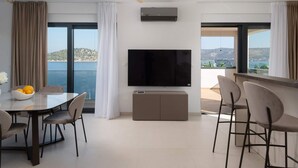 Un salon moderne doté d’un grand téléviseur à écran plat, d’un coin repas avec une table en verre et d’une vue sur la mer.
