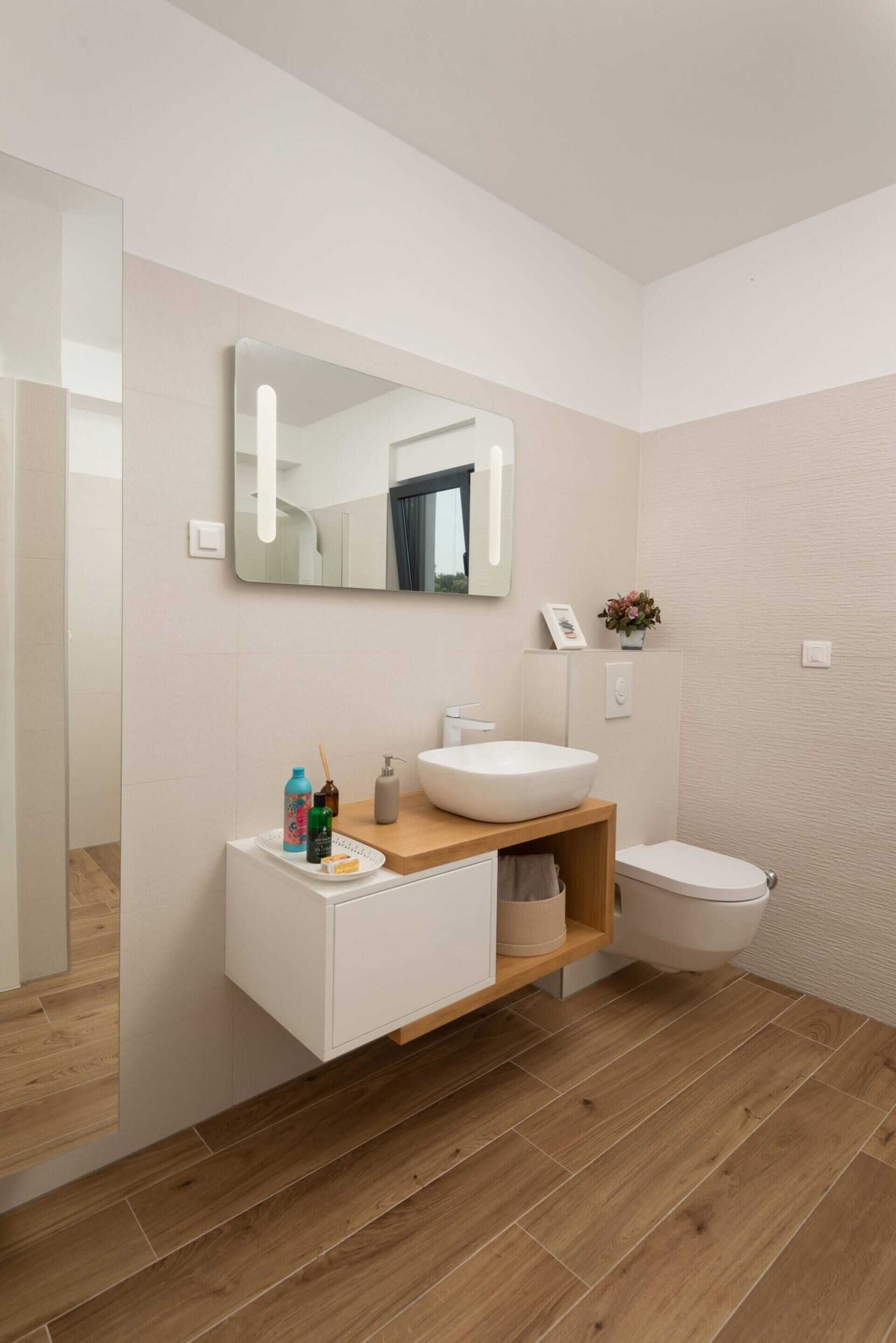 A modern bathroom with a wooden vanity, a large mirror, a white sink, and a toilet.