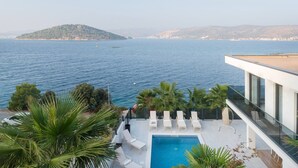 Un bâtiment moderne doté d’une piscine sur le toit, offrant une vue sur une mer calme et des collines lointaines.