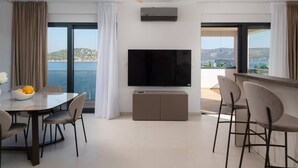 Una sala de estar moderna con un televisor de pantalla plana grande, una zona de comedor con mesa y sillas, y vista al mar.