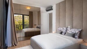 Un dormitorio moderno con una cama grande, una mesita de noche, un espejo y vistas al verde exterior.